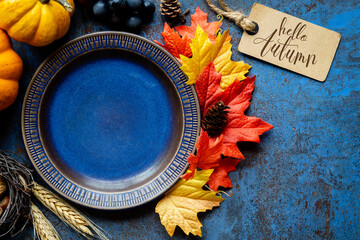 Hello Autumn concept with a dark blue plate and traditional fall decorations  - leaves, pumpkins, grapes, nuts and ponecones. Thanksgiving celebration  and harvesting