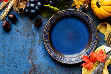 Hello Autumn concept with a dark blue plate and traditional fall decorations  - leaves, pumpkins, grapes, nuts and ponecones. Thanksgiving celebration  and harvesting with copy space