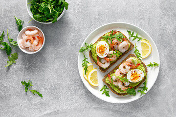 Toast with shrimps, avocado guacamole, arugula and boiled egg, top view