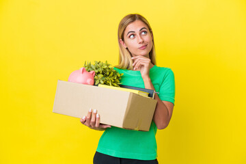 Young Uruguayan girl making a move while picking up a box full of things isolated on yellow background having doubts and thinking