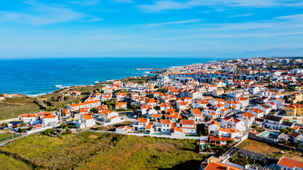 Fototapeta na wymiar Aerial view of a small European town against blue sky and Atlantic Ocean. Drone view of a beautiful European city with a hilly landscape on ocean background. Beautiful natural landscape. Portugal.