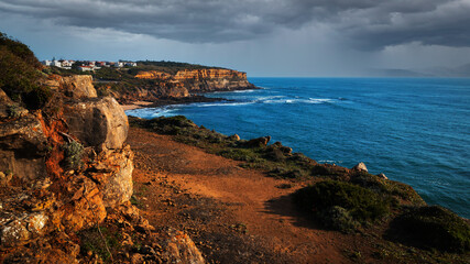 Fototapeta na wymiar Beautiful natural landscape with ocean rocky shore with rainy clouds. Scenic ocean landscape on summer rainy day. Beautiful rocky coast in Santu Isidoro with cloudy sky. Portugal. Europe.