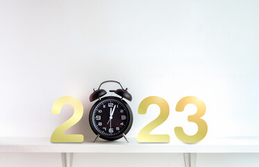 2023 Happy New year backgrounds. Golden 2023 calendar numbers with black alarm clock after midnight time on shelf on white background with copy space , Merry Christmas and Happy new year concept.