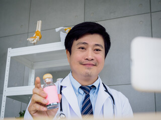 Portrait of Asian male doctor in white uniform with a stethoscope explaining about medicine in bottle, drug use, online video call and consulting patient. Healthcare medical and Telemedicine concept.