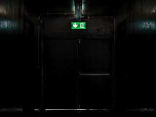 Green exit fire sign hanging on ceiling on dark mysterious corridor in building near fire exit...