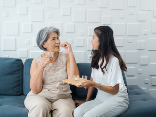 Portrait of Asian senior woman grey short hair holds pill and a glass of drinking water from young adult daughter, taken daily medicine or vitamin supplements, elderly healthcare and medical at home.