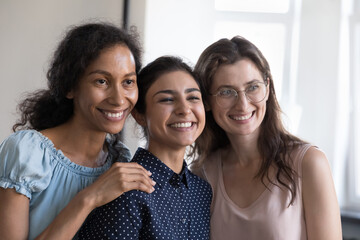Happy successful diverse business team friends women celebrating project success, looking away, hugging, posing for shooting, smiling. Office friendship, teamwork concept