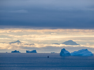 Fototapeta na wymiar Enormous icebergs seen during the midnight sun, Disko Bay north of the Artic Circle near Ilulissat, Western Greenland. In the background the mountains of Disko Island