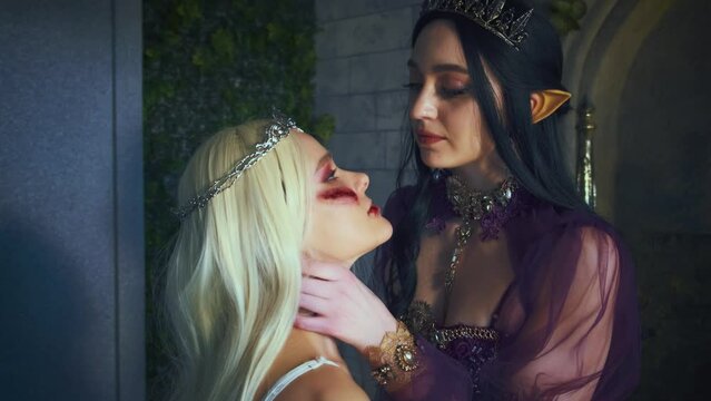 Fantasy woman evil gothic queen, strangles punishes girl princess blonde, holds hand by neck. Halloween party concept, carnival costumes, elf lady vampire pointy ears, creative medieval dress, crown