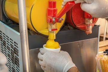 Seller pours frozen juice or serbet into a once-only glass from the machine. Close-up