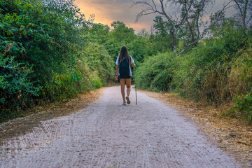 Young woman walking on the countryside hiking path.
Rear view of a girl walking on the hiking trail in the countryside. Woman with backpack hiking in extreme terrain. Nomadic lifestyle