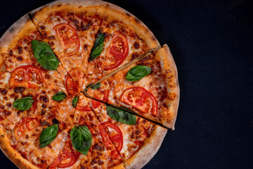 Delicious fragrant pizza-Margherita with mozzarella, tomatoes and basil on tomato sauce on black background