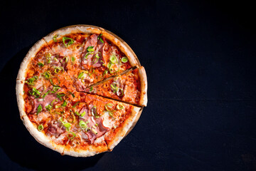 Delicious pizza with mozzarella cheese, ham, leeks on a tomato base on black background. Copy Space