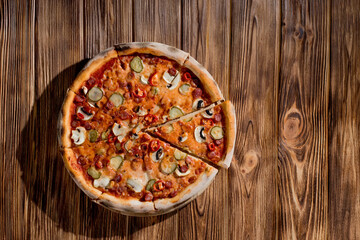 Appetizing pizza with hunting sausages, mozzarella cheese, pickled cucumbers, chili peppers on a tomato base on wood background