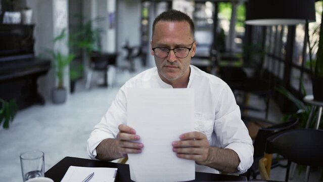 Focused adult businessman working on project, writing paper notes, sitting at caffee desk. Concentrated male professional analyzing market research information
