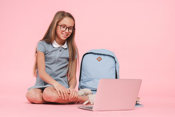 Happy caucasian young preteen schoolgirl teenage girl in uniform with bag using laptop e-learning...