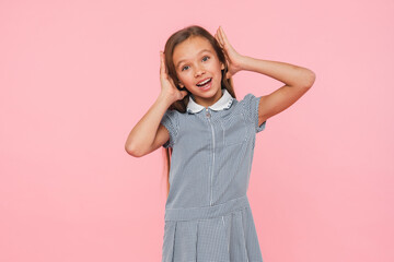 Funny impressed shocked young caucasian preteen teenage schoolgirl in blue dress looking at camera with open mouth isolated in pink background