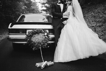 black and white photo of happy young newlywed couple near decorated retro car with plate just...