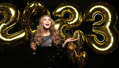 Happy gorgeous girl in stylish sexy party dress holding gold 2023 balloons, having fun at New Year's Eve Party.