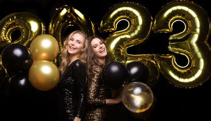 Happy gorgeous girls in stylish sexy party dresses holding gold 2023 balloons, having fun at New...