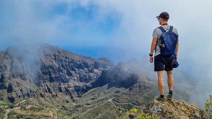 Man with backpack enjoying view on Teno mountain range near Masca village, Tenerife, Canary Islands, Spain, Europe. Fog going down the valley creates a mystical atmosphere. Remote hiking trail