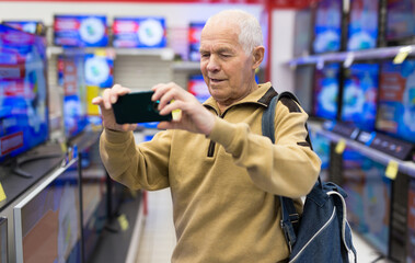 elderly grayhaired man pensioner takes a photos modern digital televisors in showroom of digital goods store