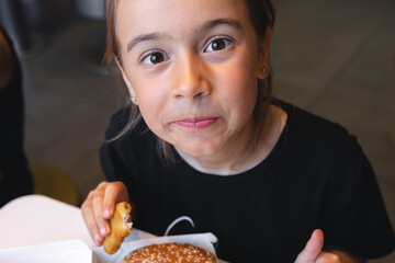 A little girl eats fast food in a cafe.