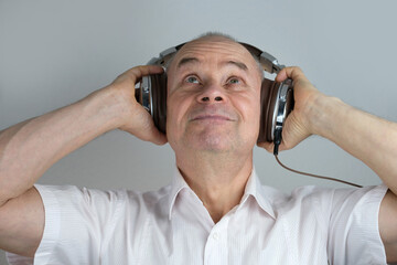 close-up of mature charismatic man 60 years in headphones listening to music with emotions on face...