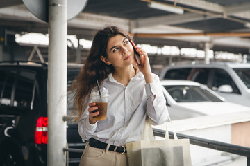 Business young woman with coffee talking cheerfully on the phone in the parking lot.