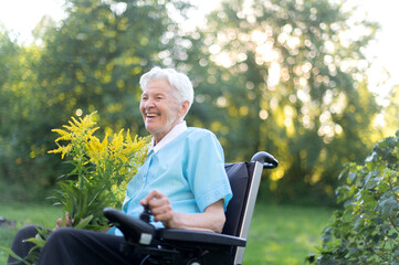 Obraz premium happy old senior woman sitting in a wheelchair and holding a bouquet of yellow wildflowers