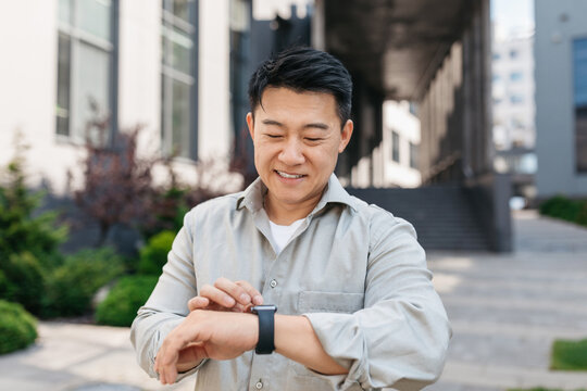 Confident asian mature man looking at watch, waiting client near modern office building, checking time outdoors - Powered by Adobe