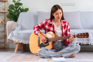 Hobby concept, Young asian woman sit on floor to playing acoustic guitar after composing new song