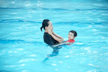 Little asian boy playing with his mother in swimming pool