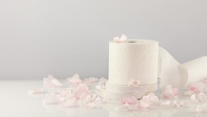 Fototapeta na wymiar Roll of white toilet paper on a white table with rose petals and copy space. White toilet tissue, Hygiene product. Restroom soft touch toilet paper. Soft focus style image, horizontal orientation