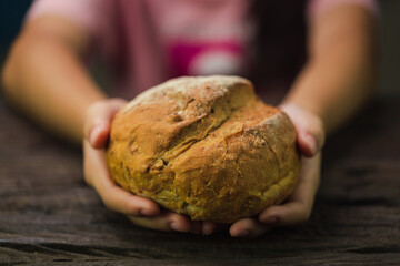 Cinematic macro shot of professional artisan baker is showing in camera just prepared fresh whole grains white bread taken out of oven in rustic bakery kitchen.