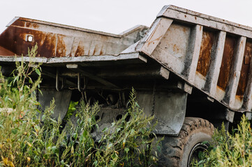 Old, broken rusty abandoned car big truck, overgrown with bushes, green grass stands outdoors.