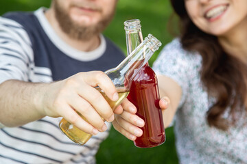 A young man and woman drink drinks in glass bottles at a picnic.