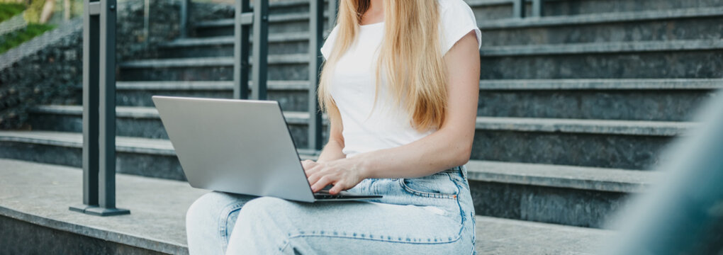 female student sitting with laptop on stairs near university smiling and studying