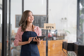 Young asian woman coffee shop owner wearing apron holding digital tablet ready to receive orders.