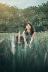 Fototapeta na wymiar Young asian black hair woman in green dress smiling chin up sitting among meadow closed eye and feeling fresh. Portrait of woman in summer with grass field.