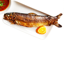 Baked mullet on a plate with lemon. Fried fish with a golden crust with tomato sauce