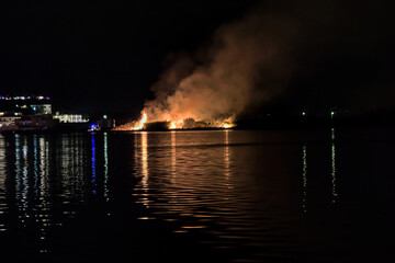 Naklejka na ściany i meble Fire on the shore of the lake, burning a lot of vegetation.
