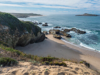 View of empty Praia do Sissal sand beach with ocean waves and sharp rock and cllifs at wild Rota Vicentina coast near Porto Covo, Portugal.
