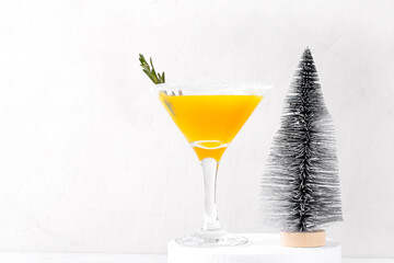 Yellow cocktail in martini glass decorated with sugar border and rosemary. Christmas drink with mango on white
