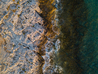 Aerial drone view of sea and rocks on the beach. Beautiful natural rocky beach at summer. Waves crushing on wild beach at sunset. Coastline. Transparent sea water