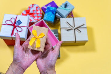 Gift box, Top view shot of female hands holding a small gift with yellow ribbon. Small gift in the hands of a woman indoor. Shallow depth of field with focus on the little box
