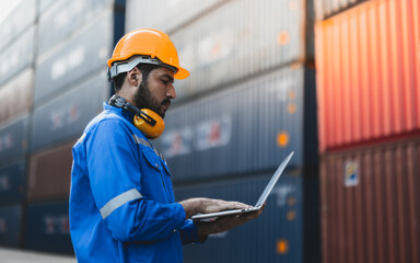 Container operator holding a laptop while doing his daily routine inspection. He is wearing a yellow hard hat and blue reflect jacket while working in container yards.