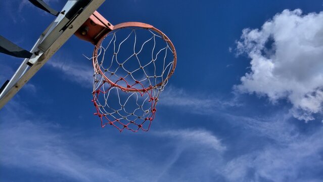 Under a basketball hoop with deep blue sky cloud in background