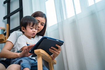 Asian baby boy sitting on his mother lap and playing tablet in the living room.