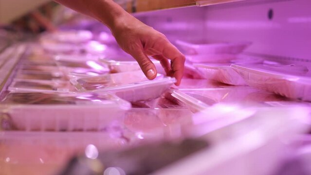 Refrigerated shelf in a store with chilled meat packed in plastic packaging. The customer chooses fresh meat to prepare a delicious meal for the whole family. Consumption of meat products.